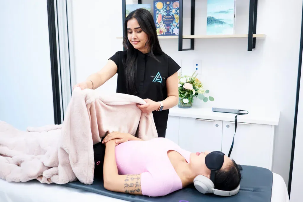An Ageless Living practitioner settling a patient under a blanket before a recovery session in the biohacking suite