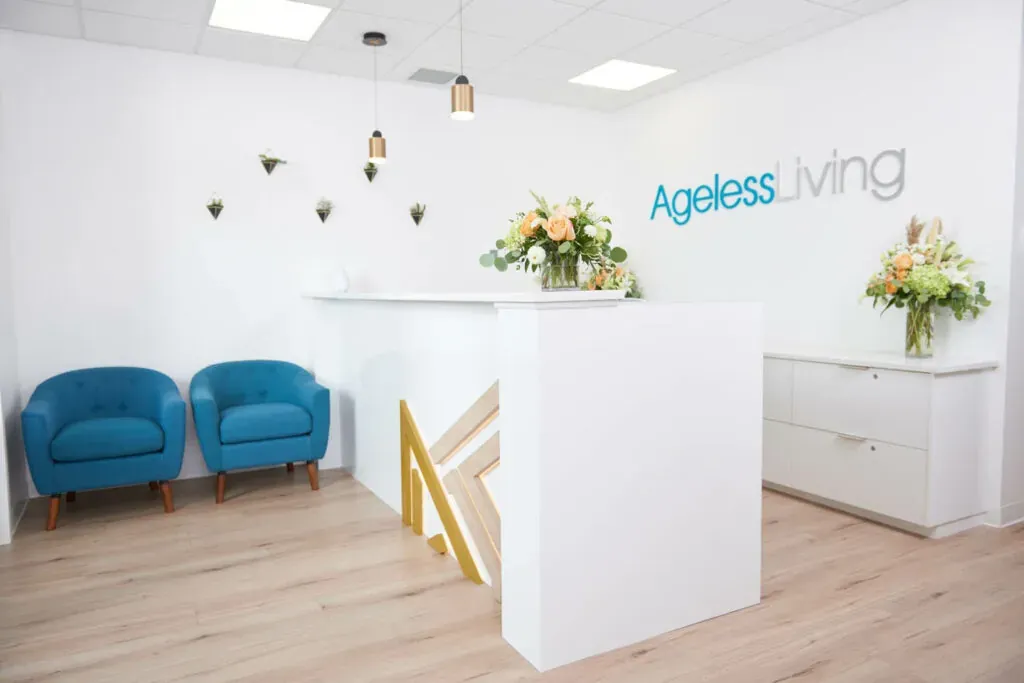 The bright reception area of an Ageless Living clinic with teal chairs and a white front desk