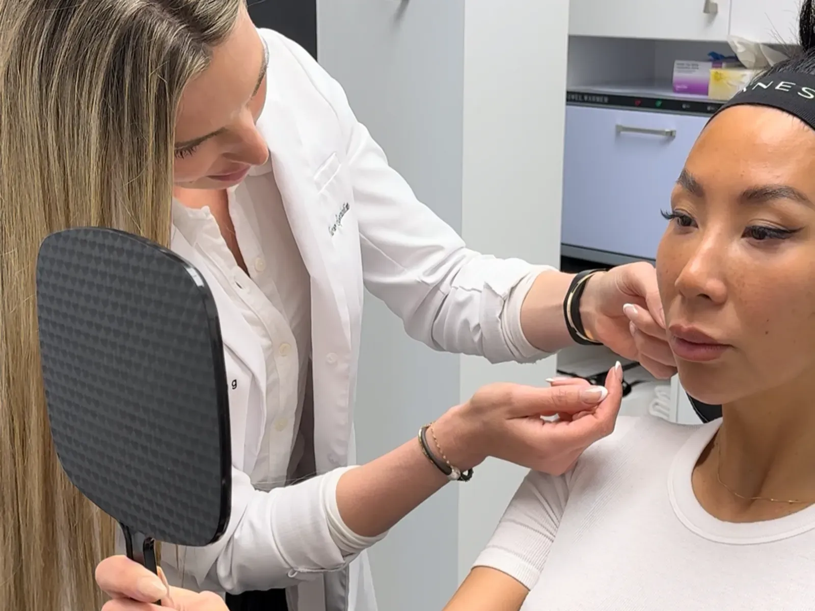 An Ageless Living practitioner checking a client's skin as she looks in a hand mirror