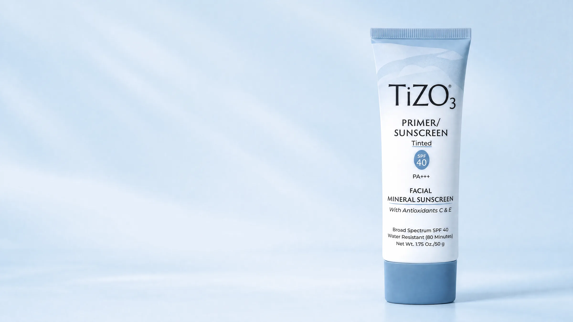 A tube of TiZO tinted primer sunscreen against a pale blue sky